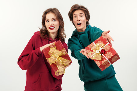 Two cute teenagers - a girl and a boy - dressed in green and red sweatshirts, pose joyfully with gifts. White studio background. Merry Christmas and Happy New Year!の写真素材