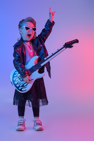 Cool little girl - rock star, rock musician. Full length portrait of a pretty girl in black clothes and a black leather jacket playing the electric guitar in the studio.の写真素材
