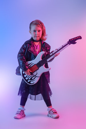 Full length portrait of a pretty girl in black clothes and a black leather jacket playing the electric guitar in the studio. Cool little girl - rock star, rock musician.の写真素材