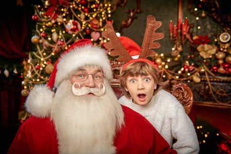 Portrait of a kind Santa Claus and a happy child boy who are sitting in a chair in a fabulous Christmas room.の写真素材