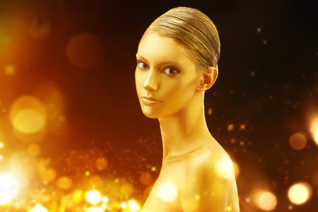 Holiday luxury beauty concept. Portrait of a beautiful girl with perfect golden skin and hair surrounded by magical golden lights. Golden Christmas lady. Copy space.の写真素材