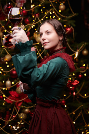 Christmas in vintage style. An elegant aristocratic lady in home clothes drinks wine next to a Christmas tree richly decorated for the holiday. The heroine of the novel of the 19th - early 20th century.の写真素材