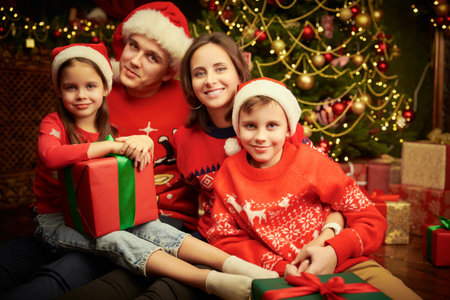Family Christmas and New Year. A happy family of parents and two children are sitting near the Christmas tree with gifts in their hands and smiling.の写真素材