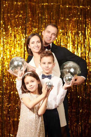 Family evening fashion. Beautiful happy family of parents and two children posing in festive outfits against a shiny gold foil background. Celebrating Christmas and New Year.の写真素材