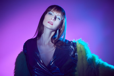 Evening makeup and hairstyle. Portrait of a bright brunette girl with sparkling silver makeup and shiny clothes with sequins in mixed color light. Brilliant party style.の写真素材