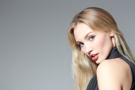 Portrait of a stunning young blonde woman with elegant makeup and sensual lips. Feminine beauty. Makeup and cosmetics. Hair care. Studio shot on a grey background with copy space.の写真素材
