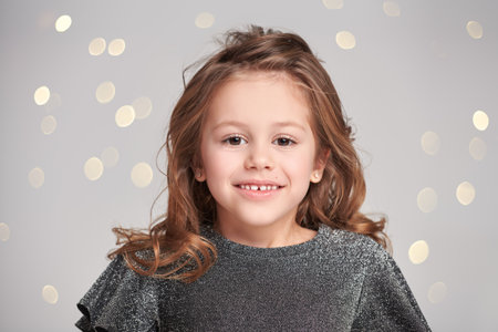 Happy cute little girl laughs cheerfully while looking at the camera. Festive background with twinkling lights.の写真素材