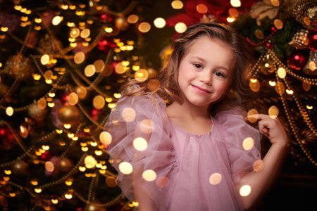 A beautiful little girl in a fluffy festive dress smiles happily while standing in a fairytale Christmas setting. Children's Christmas and New Year. Evening fashion for children. Copy space.の写真素材