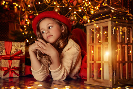 Waiting for a miracle. A cute little girl lies under the Christmas tree on Christmas night by the light of a lantern and quietly dreams about something. Retro style.の写真素材