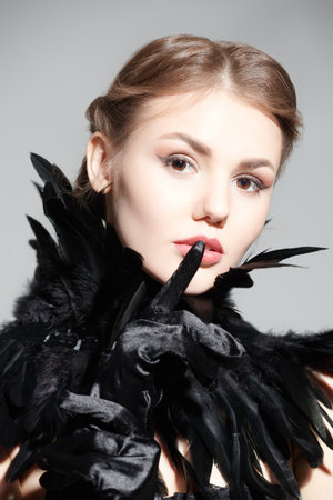 Fashion shot. Profile portrait of a beautiful dark-haired girl with evening make-up, wearing a black feather collar. Studio portrait on a gray background.の写真素材