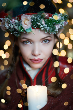 Winter Christmas tales. A fabulously beautiful elf girl in winter clothes covered with snow looks to the camera holding a candle. Magic. Fantasy.の写真素材