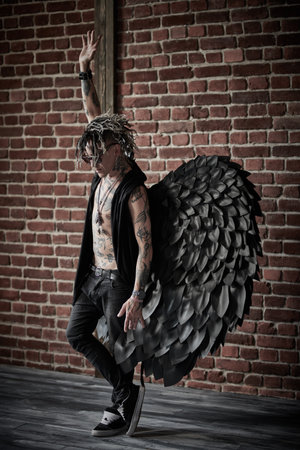 Full-length portrait of a cool rock musician in a black angel costume against a brick wall. Artist. Rock style.の写真素材