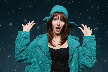 Portrait of an attractive brunette young woman model posing in a bright green fur coat and green knitted hat on a green studio green background. Winter Christmas fashion style. Copy space.の写真素材