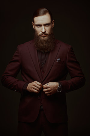 People and characters. Portrait of a stylish mature man with a long beard posing emotionally in an elegant suit against a black studio background.の写真素材