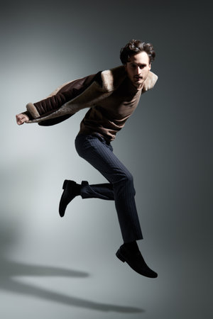 Fashion shot. Full-length portrait of a cool male fashion model posing in classic clothes and sheepskin coat in motion. Grey studio background.の写真素材