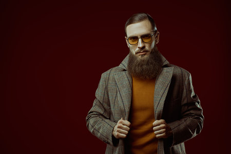 Men's fashion. An impressive well-groomed man with a beard and long hair poses in a fashionable coat and glasses. Studio portrait. Barbershop for men. Copy space.の写真素材