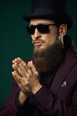 A respectable gentleman with a long beard, dressed in an elegant three-piece suit and a top hat, poses against a black background. Retro style. Men's fashion.の写真素材