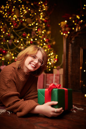 Merry Christmas and Happy New Year! A pretty red-haired girl lies under the Christmas tree with a gift and smiles joyfully.の写真素材