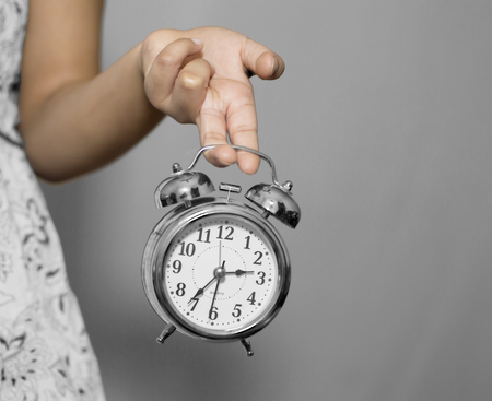 A girl holding silver color alarm clock with fingers.の写真素材