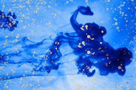 Blue ink in water. Golden dust and drops on it. Alcohol ink fluid abstract texture fluid art with gold glitter and liquid with shades.の写真素材