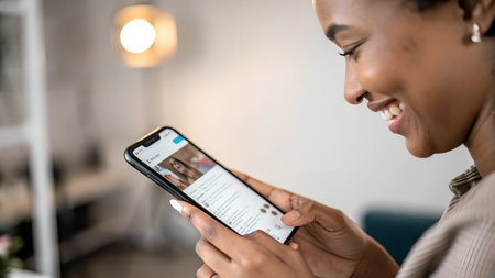 Closeup of smiling african american woman using smartphone at homeの素材