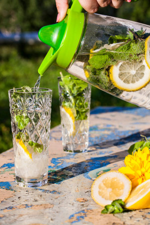 Lemonade pitcher with lemon, mint and ice on garden table