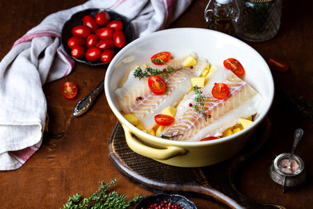 raw cod fillet with potatoes and tomatoes in ceramic baking dish