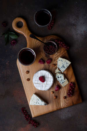 Different kinds of cheese on the wooden board with berriesの写真素材