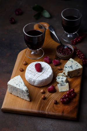 Different kinds of cheese on the wooden board with berriesの写真素材