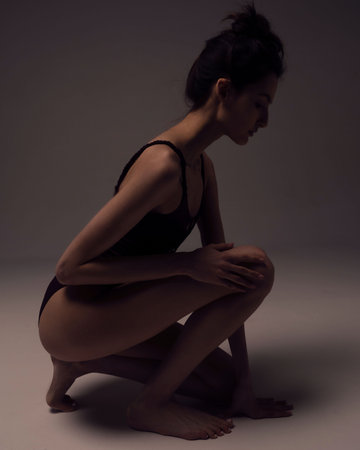 A beautiful young girl in a black bodysuit with long sleeves sits on a light background.の写真素材
