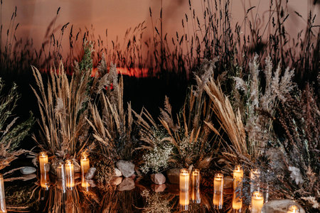 Illuminated by candles, a tranquil scene features natural grasses, stones, and a twilight reflection, creating a serene, atmospheric backdrop of beauty and calmness.の写真素材