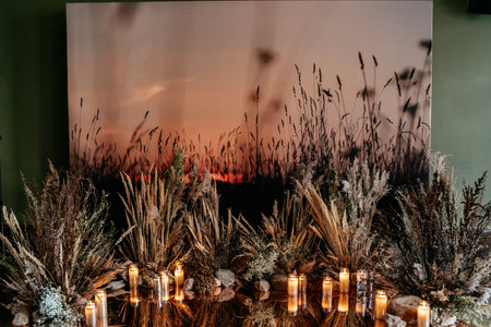 A tranquil evening setting featuring tall grasses silhouetted against a colorful twilight horizon. candle arrangements enhance the serene, natural ambiance.の写真素材
