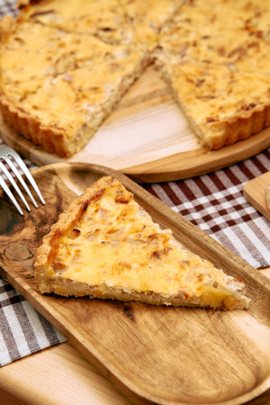 A slice of savory onion tart rests on a rustic wooden platter. the golden crust and flavorful...