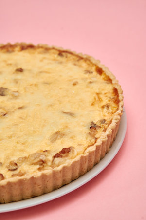 A savory quiche featuring cheese and onions sits invitingly on a white plate against a pink surface,...
