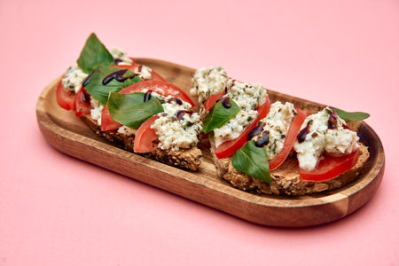 Fresh bruschetta topped with tomatoes, basil, and cheese sits on a wooden platter against a pink background, offering a vibrant and delicious appetizer option.の写真素材
