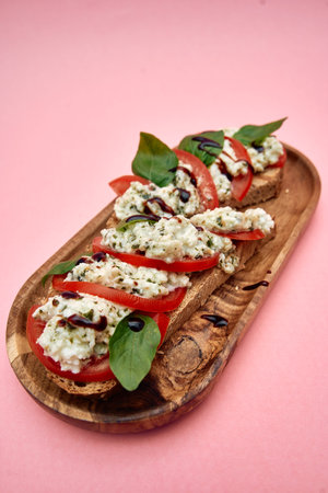 Fresh tomato bruschetta topped with creamy cheese and basil leaves, arranged on a rustic wooden platter. a vibrant Italian appetizer ideal for gatherings.の写真素材