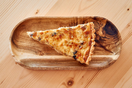 A slice of rustic quiche, artfully placed on a wooden platter, showcases its golden crust and rich...