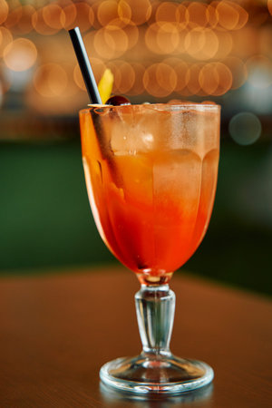 A vibrant citrus cocktail garnished with a cherry and served with a straw in an elegant glass,...