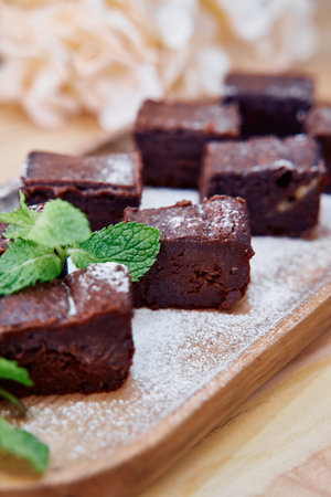 Rich chocolate brownies are garnished with fresh mint leaves and a dusting of sugar, elegantly...