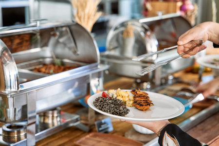 A person serves grilled chicken and lentils using tongs at a buffet, highlighting a professionally...