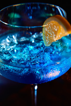 A vibrant blue cocktail garnished with a lemon slice and ice cubes, served in an elegant glass under...