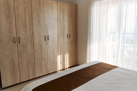 Sunlight gently illuminates a cozy bedroom featuring a wooden wardrobe and bed, creating an inviting...