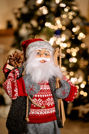 A cheerful santa figurine in a red sweater and glasses holds skis, standing against a sparkling Christmas tree background, capturing the festive holiday spirit.の写真素材