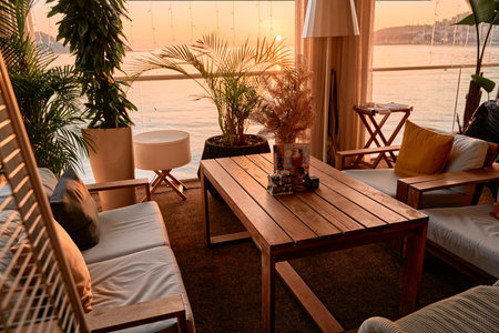 A cozy balcony setting overlooking a serene sunset by the water, featuring comfortable seating, lush...