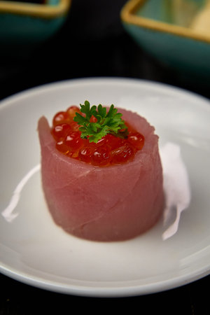 A Delicate Sushi Creation Featuring Fresh Tuna and Vibrant Salmon Roe Served on a Simple White Plate...
