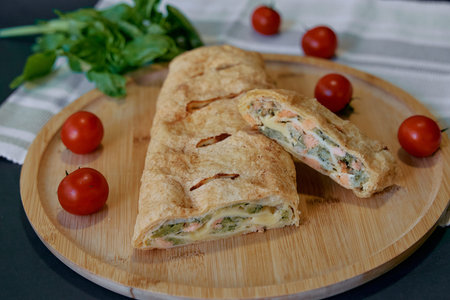 Savory Pastry Roll Filled with Fresh Vegetables and Cheese on a Wooden Plate Surrounded by Cherry...