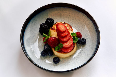 A Colorful Culinary Delight Featuring a Delicious Dessert of Fluffy Cake, Fresh Berries, and Garnishing Mint Leaves in a Beautiful Bowl Settingの写真素材