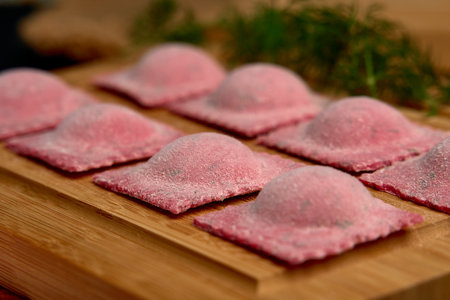 Artisanal Pink Ravioli on Wooden Board Surrounded by Fresh Herbs and Accents of Flour Ready for Cooking and Culinary Exploration in a Rustic Kitchen Environmentの写真素材
