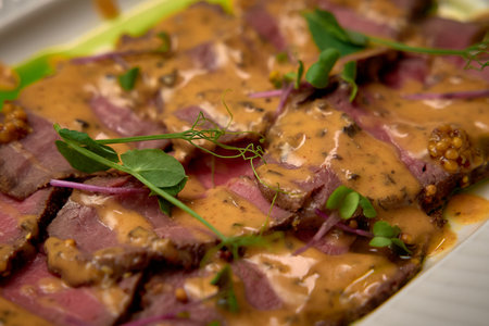 Deliciously Seared Beef Slices Topped with a Creamy Sauce and Fresh Microgreens on a White Plate, Perfect for Gourmet Dining Experiences at Homeの写真素材