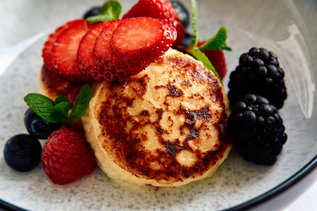 A Delightful Plate of Fluffy Pancakes Topped with Fresh Berries Including Strawberries, Raspberries, and Blueberries, Garnished with Mint Leaves for an Inviting Presentationの写真素材